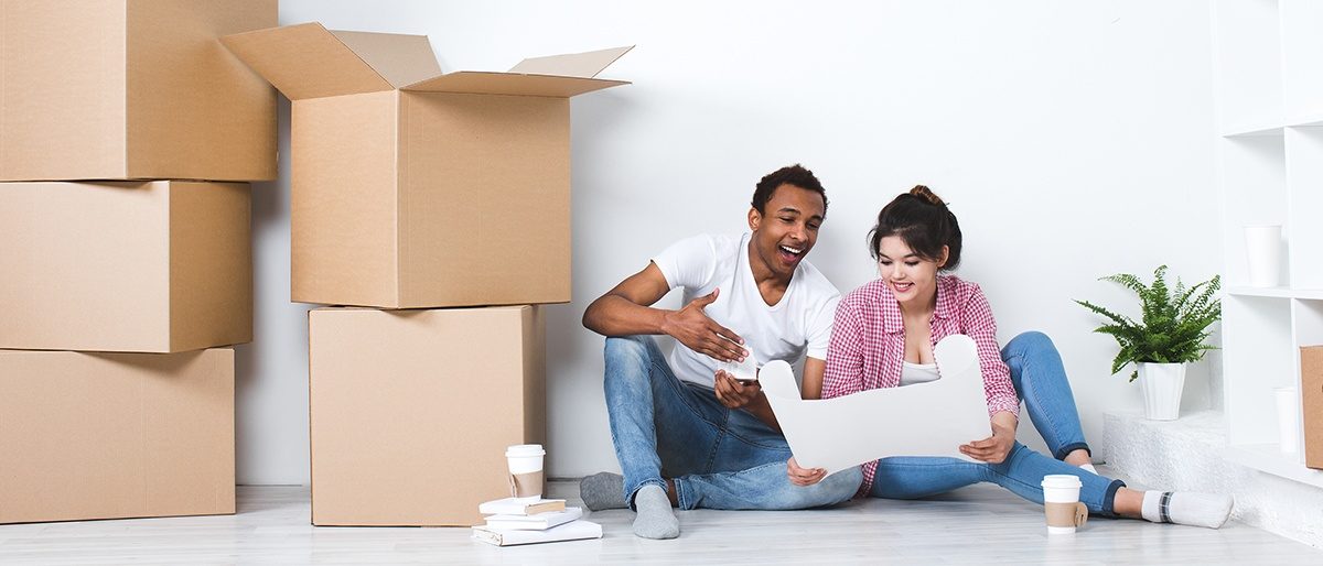 happy couple sitting on the floor looking at a floor plan surrounded by boxes